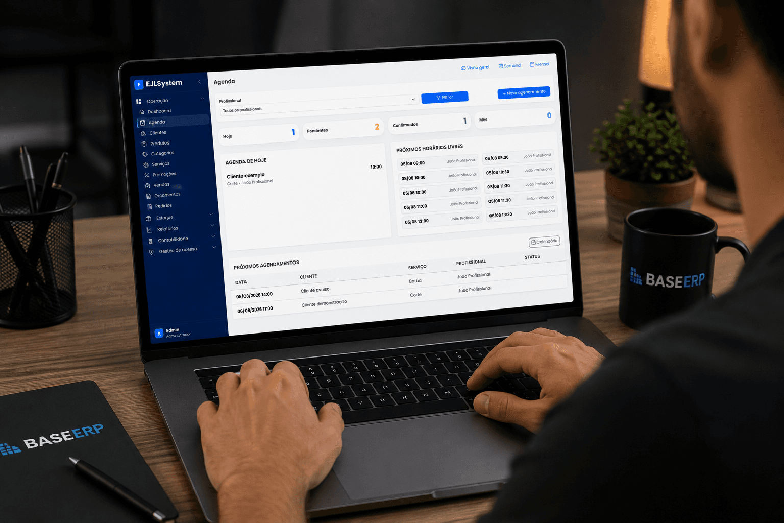 Painel de agenda do sistema EJL aberto em um notebook, com caneca e caderno da marca Base ERP na mesa